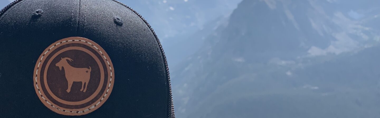 A close up of a blue OneGoat baseball hat in front of mountains in Colorado