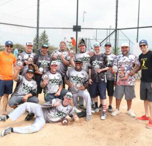 A mens softball team holding trophies in front of the home plate
