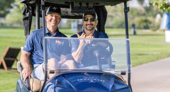 Two men smiling driving a golf cart on the golf course